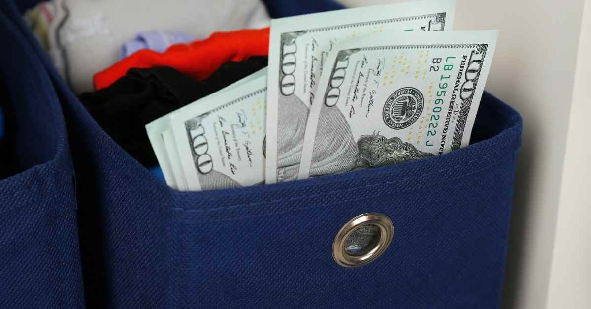 Hundred dollar bills that seem to be stuffed in a container filled with socks and other laundry items